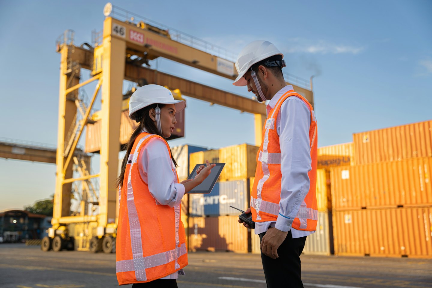 Due operatori della logistica discutono delle operazioni portuali con container e gru.
