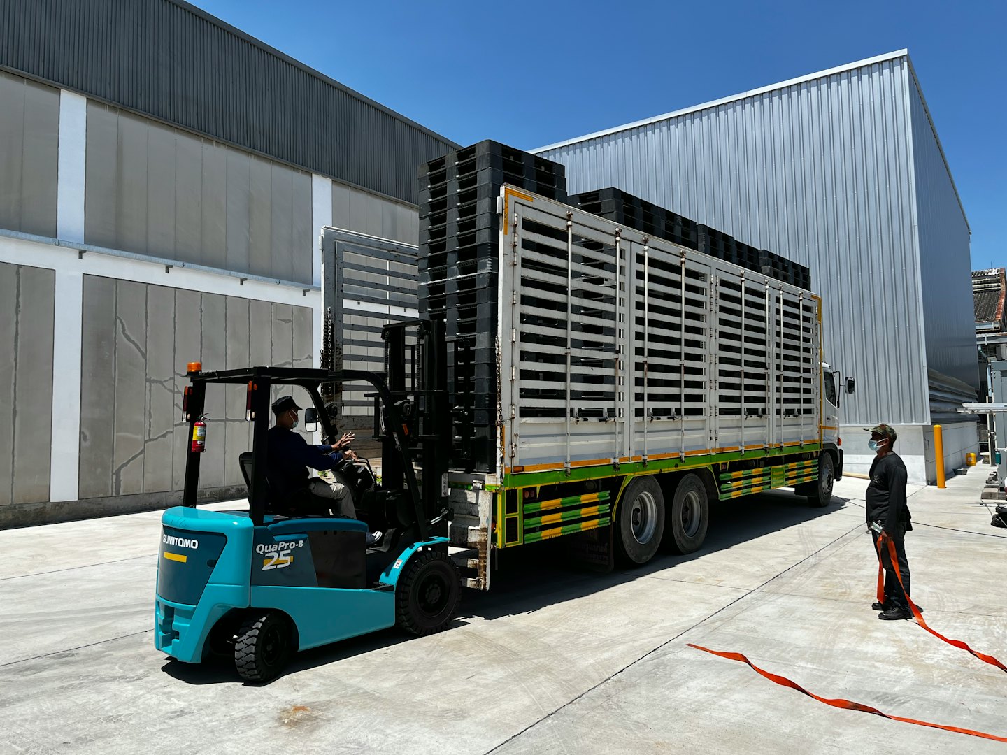 Un operaio guida un muletto color petrolio che carica pallet su un camion.