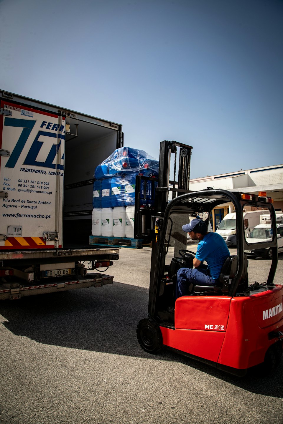 Autista in divisa blu guida un muletto mentre carica barili su un camion.
